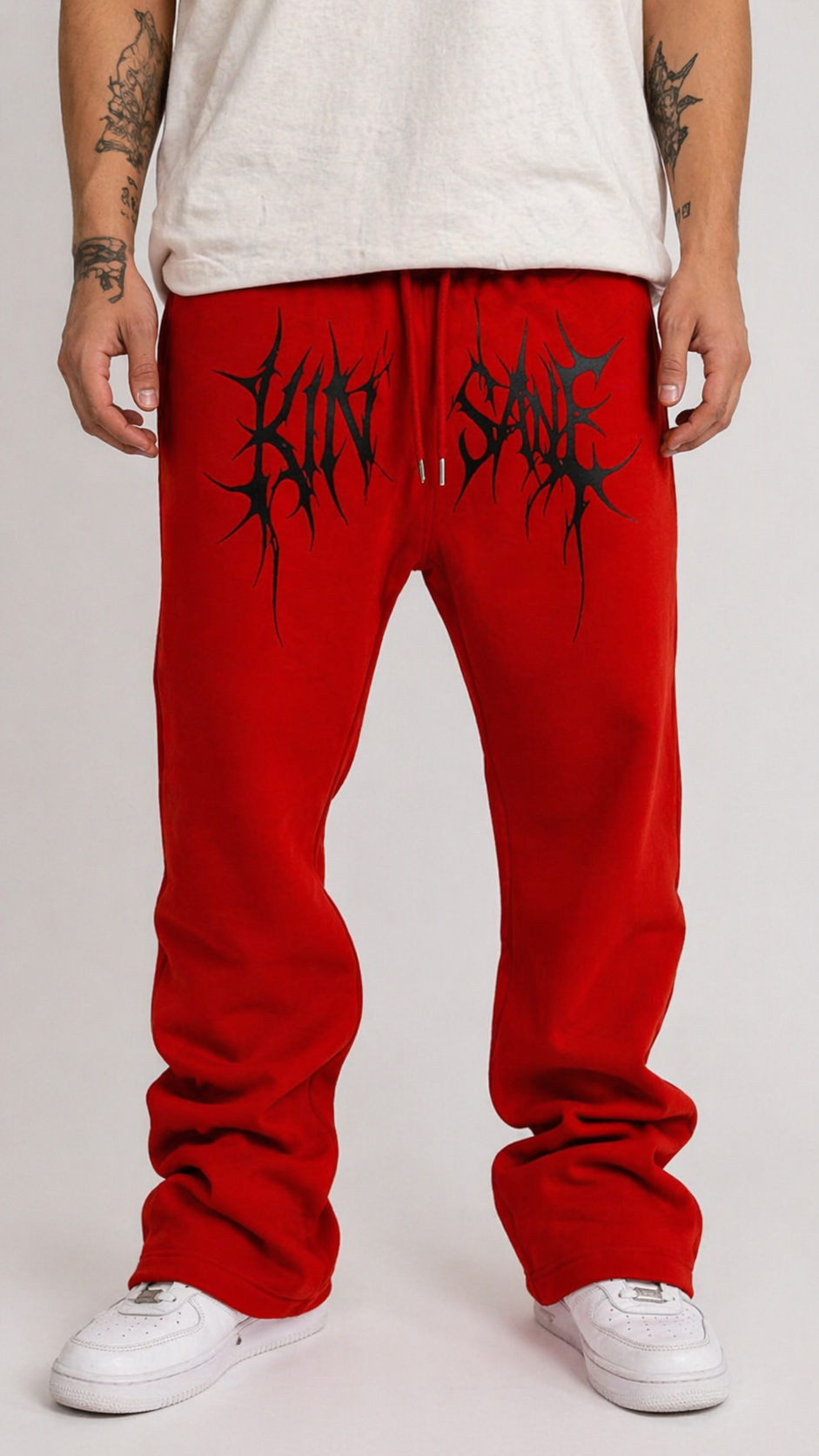 Man wearing Red stacked sweatpants with black tribal lettering across the middle reading “KINSANE” 