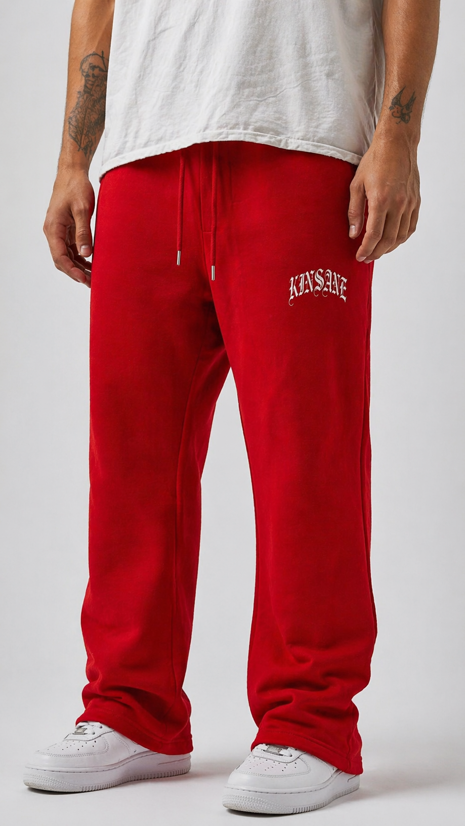 Man wearing Red stacked sweatpants with white lettering reading “KINSANE” on the right side 