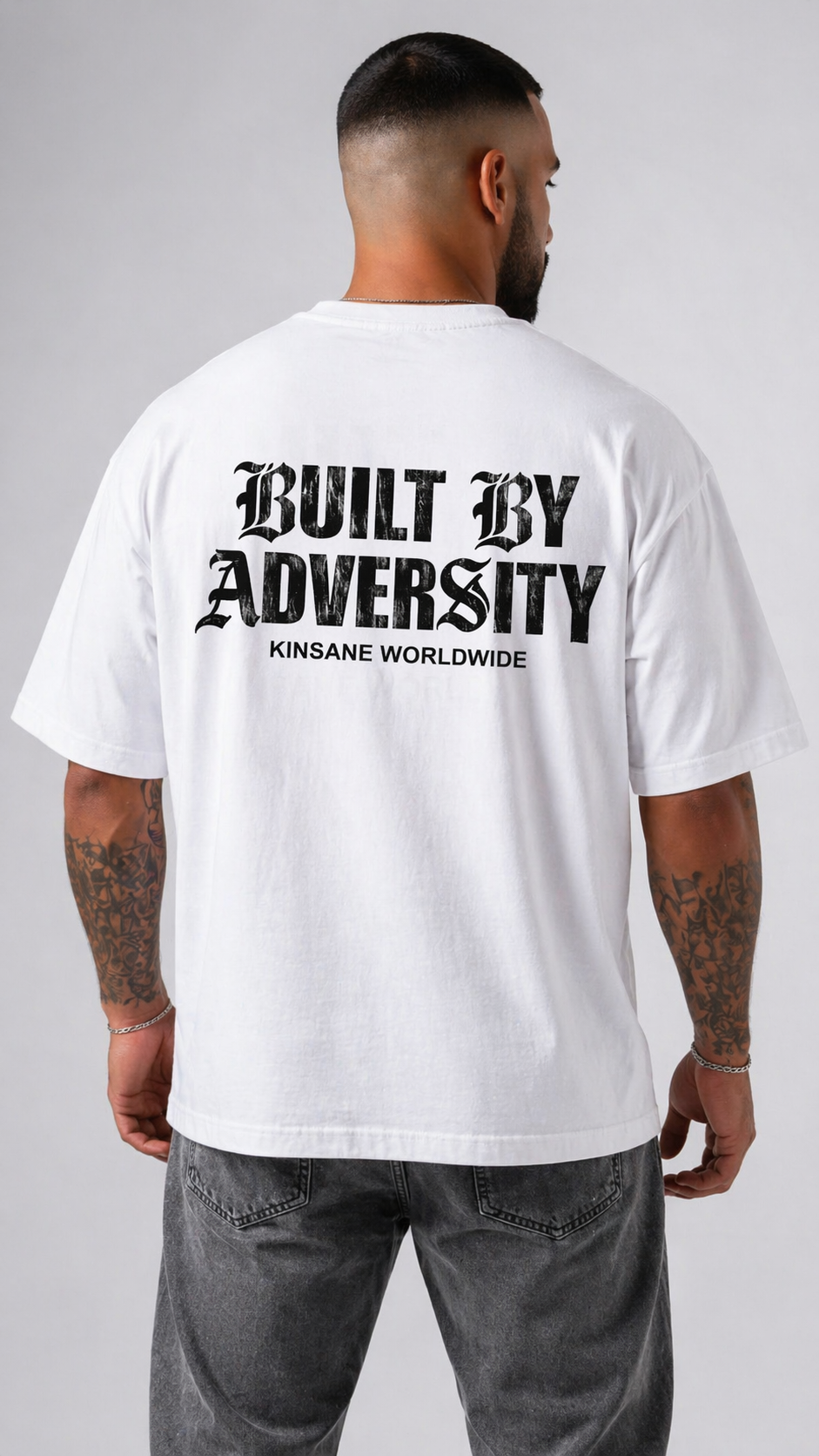Back view of a man wearing a white t shirt with black text reading “BUILT BY ADVERSITY KINSANE WORLDWIDE” 