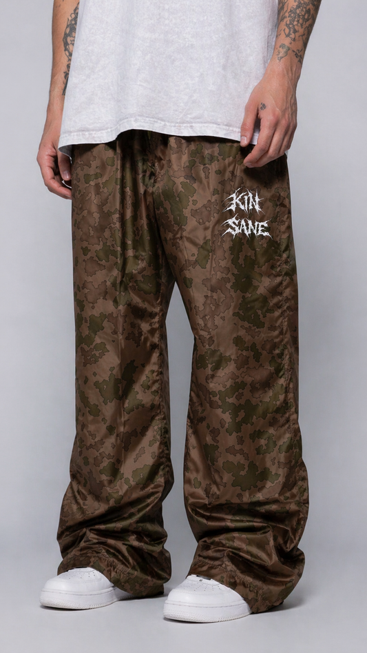 Ma wearing Brown camo sweatpants with green drawstrings and white text reading “KINSANE” on the left leg 