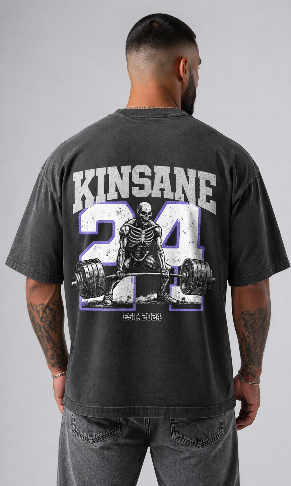 Back view of a man wearing a gray t shirt with white logo of a skeleton lifting weights and blue outlined “24” and white text reading “KINSANE” and “est 2024” 