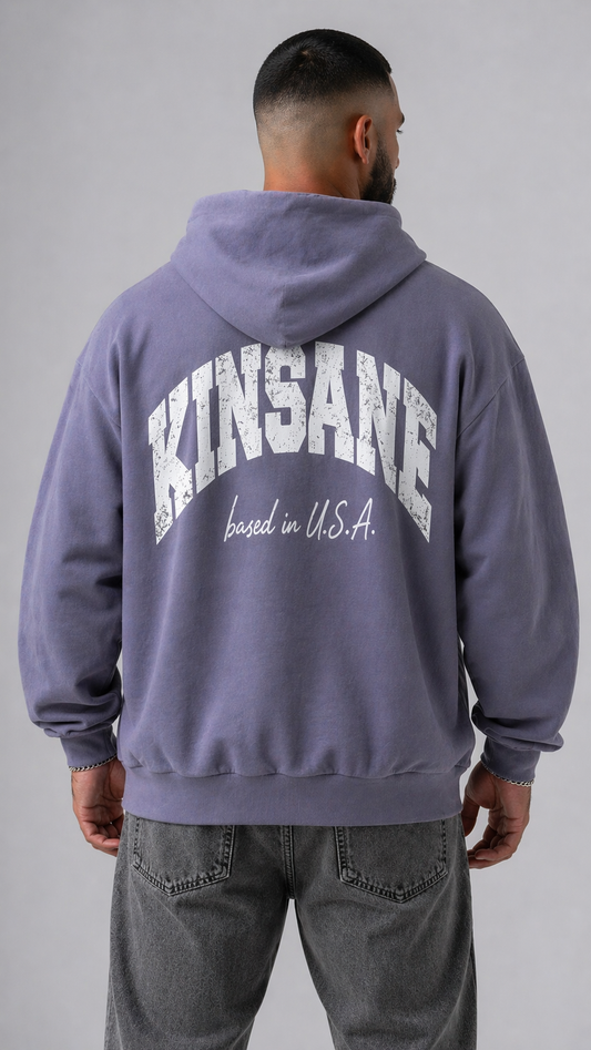 Back view of a man wearing a light blue hoodie with white text reading “KINSANE BASED IN U.S.A.” 
