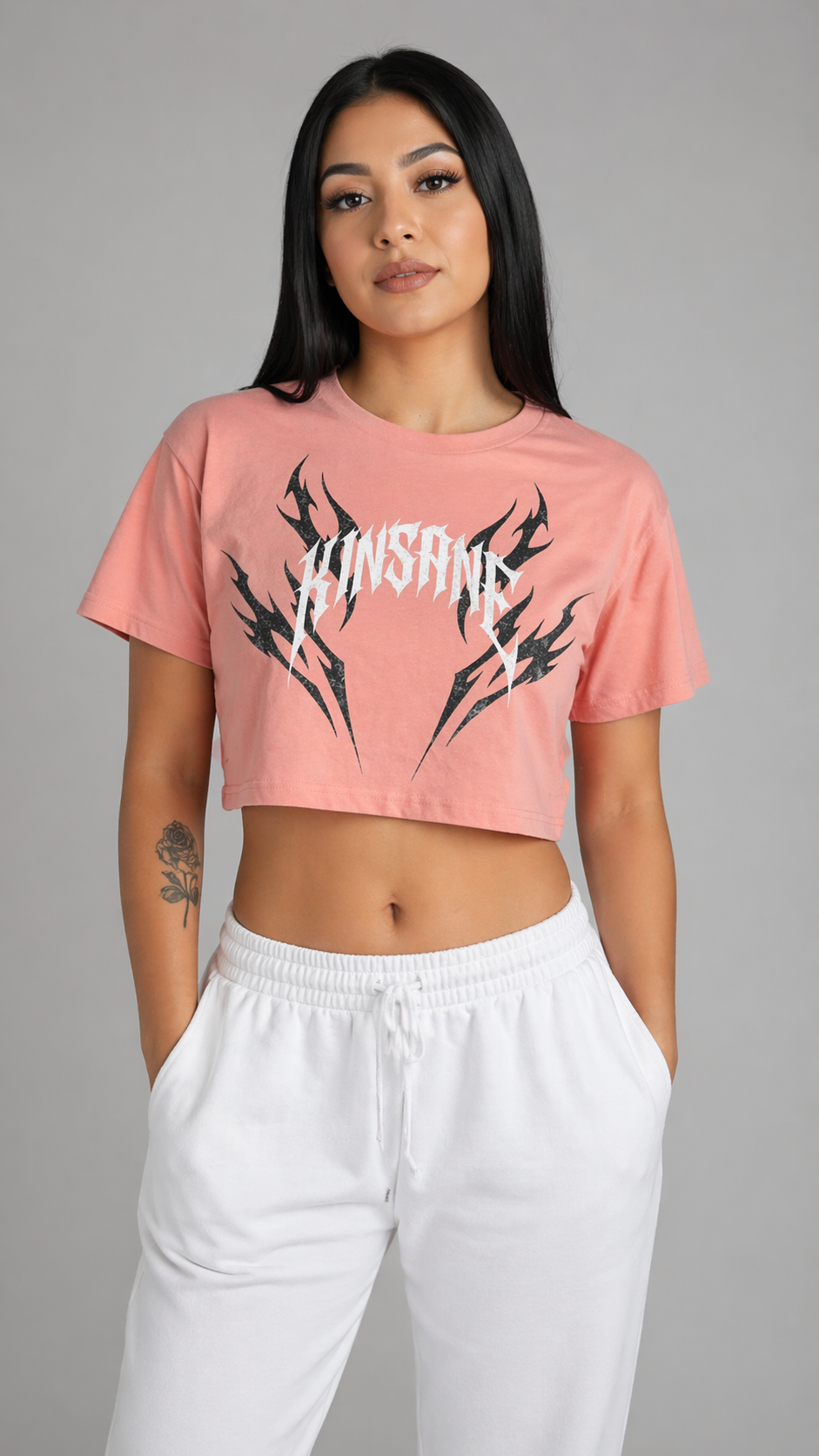 Girl wearing pink crop top T-shirt with black tribal designs and white lettering reading “KINSANE” 