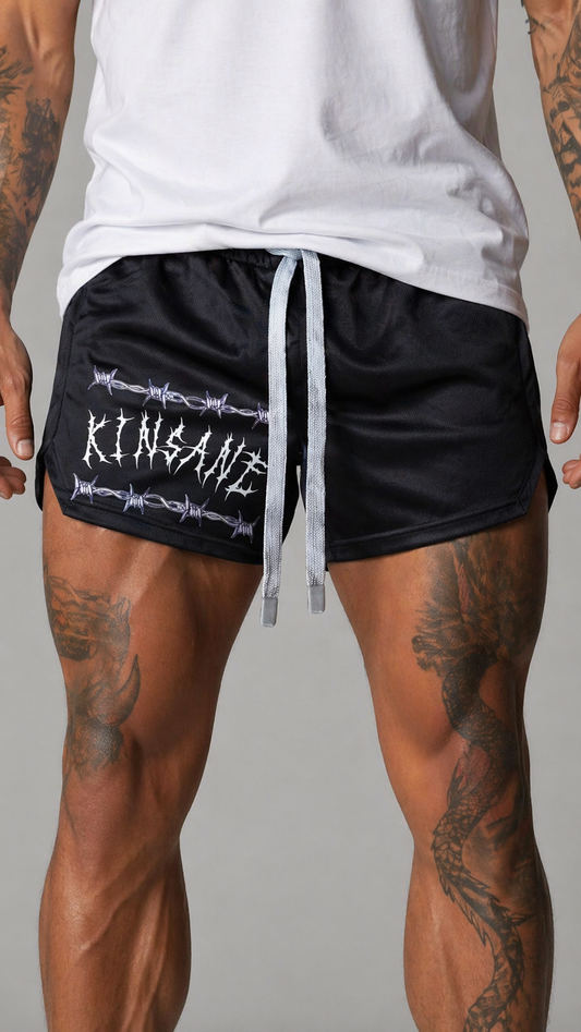 Man wearing Black athletic shorts with elastic waistband and grey drawstrings with white tribal lettering reading “KINSANE” surrounded by barbed wire on the right leg