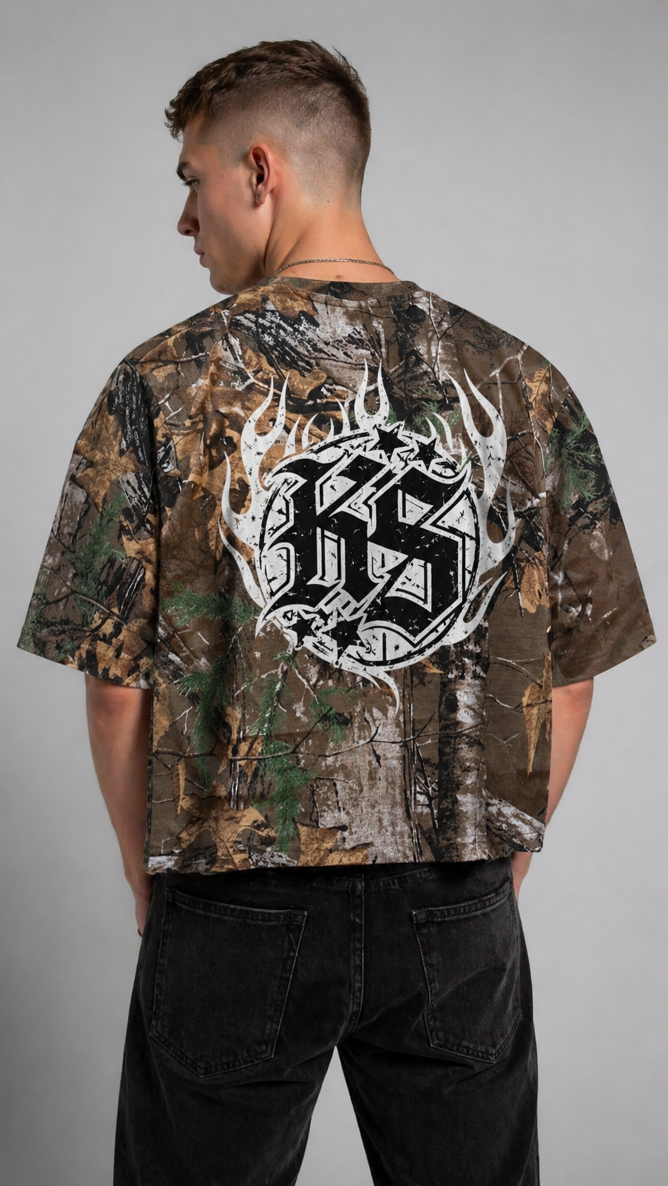 Back view of a man wearing a camouflage shirt with a white logo in flames and black letters reading “KS” 