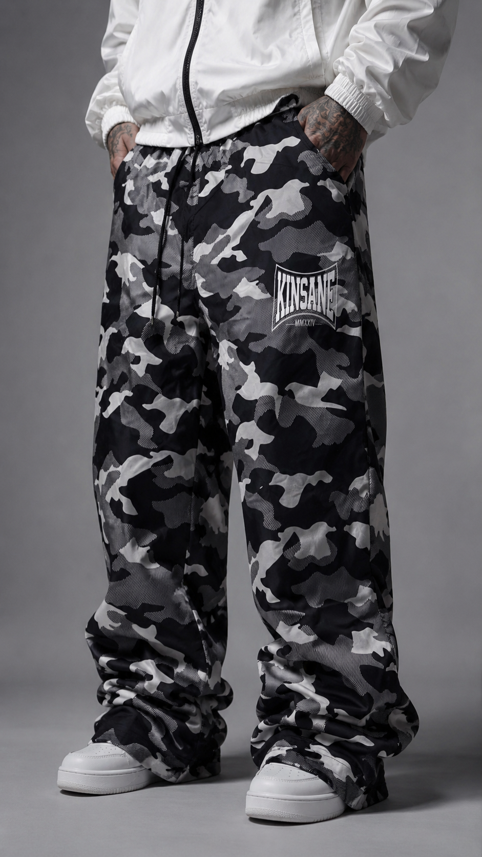 Man wearing Camo baggy sweatpants with white logo lettering on the right side reading “KINSANE MMXXIV” 