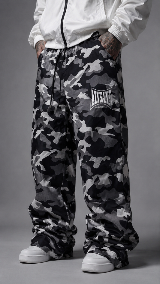Man wearing Camo baggy sweatpants with white logo lettering on the right side reading “KINSANE MMXXIV” 