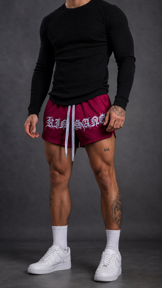 Man wearing Dark red athletic shorts with elastic waistband and gray drawstrings with white tribal lettering reading “KINSANE” across the front 