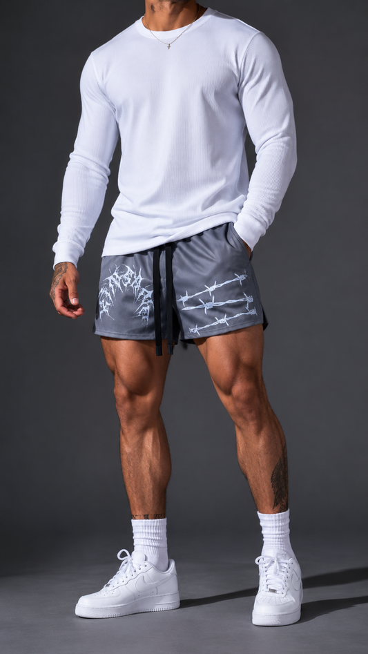 Man wearing gray athletic shorts with black drawstrings and white text reading “KINSANE” on the left side and white barbed wire design on the right side 