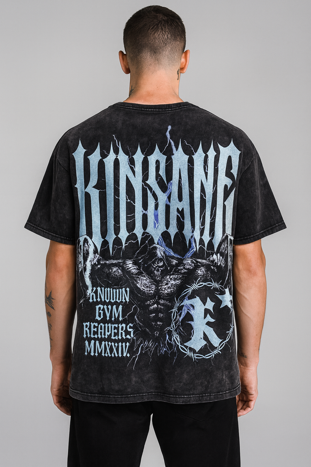 Back view of a man wearing a black acid washed t-shirt with a reaper lifting weights and silver spiked lettering reading “KINSANE” and silver lettering reading “KNOWN GYM REAPERS” 