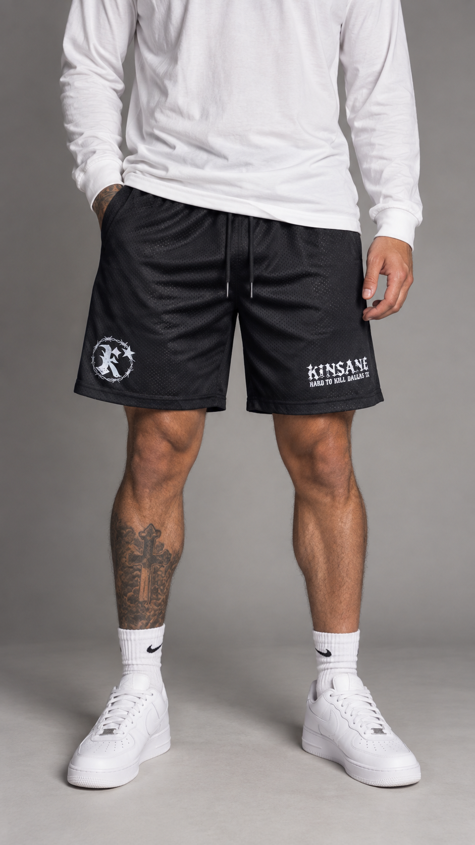 Man wearing Black mesh shorts with black drawstrings and white logos on both sides reading “KINSANE HARD TO KILL DALLAS TX” and “K” 