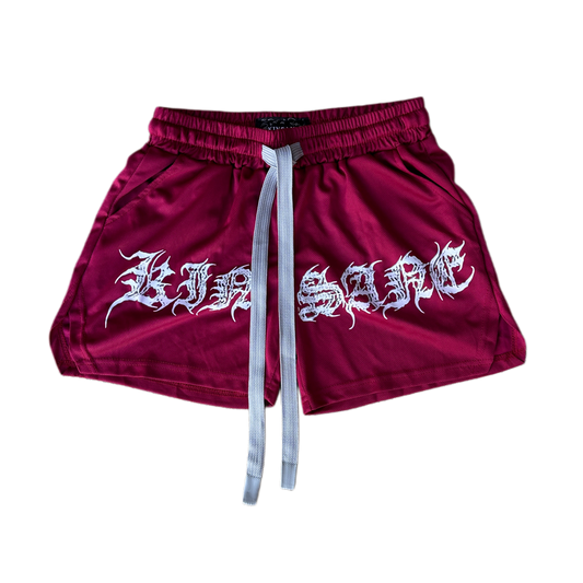 Dark red athletic shorts with elastic waistband and gray drawstrings with white tribal lettering reading “KINSANE” across the front 