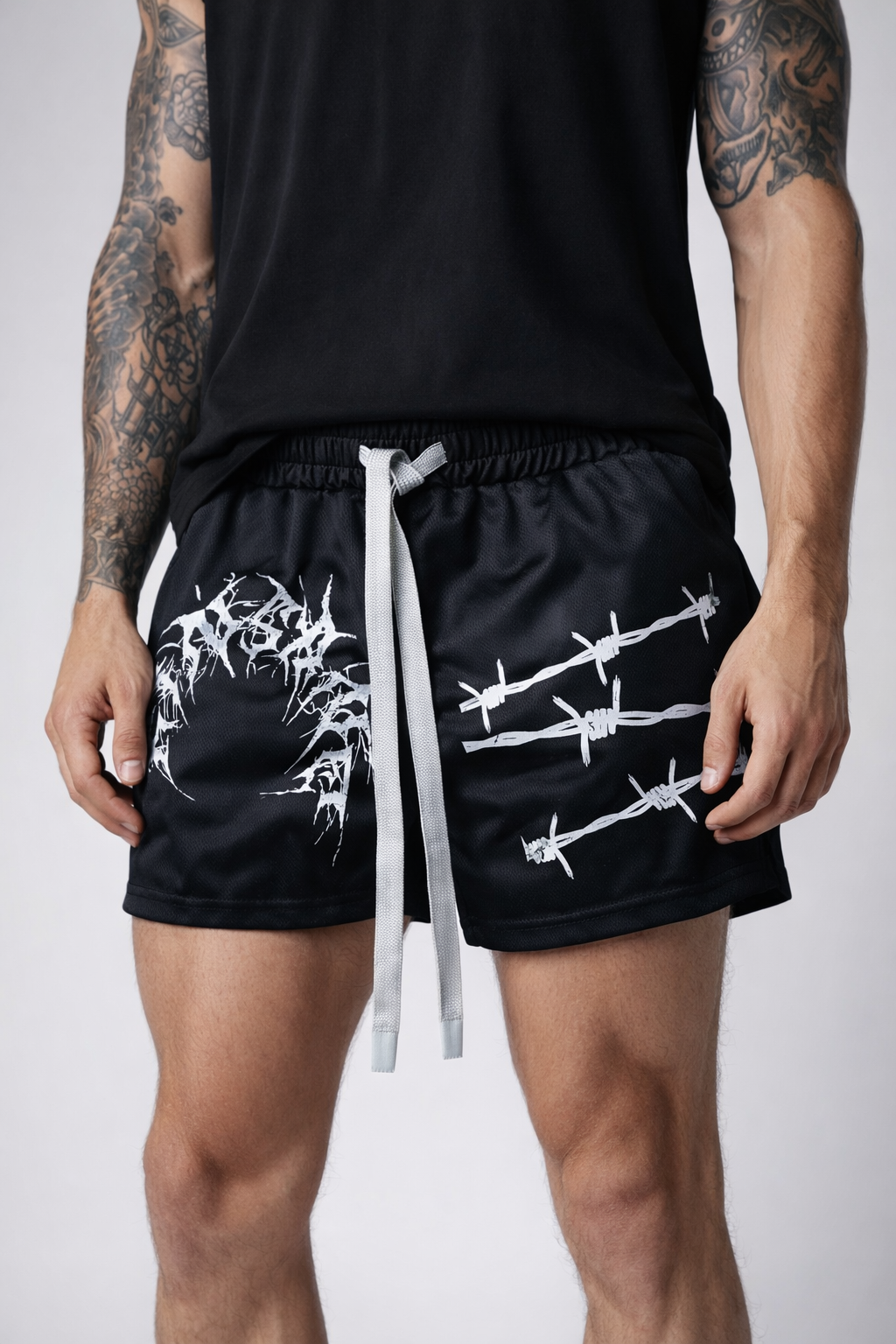 Man wearing Black athletic shorts with elastic waistband and gray drawstrings and white tribal lettering reading “KINSANE” on the right leg and white barbed wire design on the left leg 