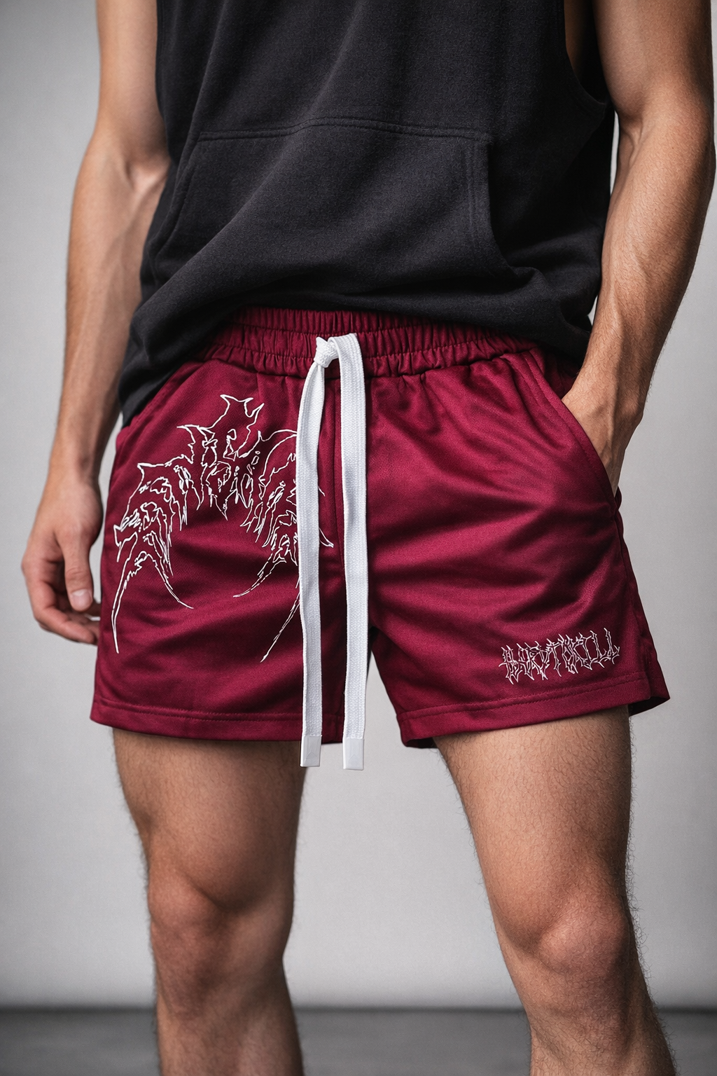 Man wearing Dark red athletic shorts with elastic waistband and white drawstrings with white outlined tribal lettering reading “KINSANE” on the right leg and white tribal outlined lettering reading “HARDTOKILL” on the left leg