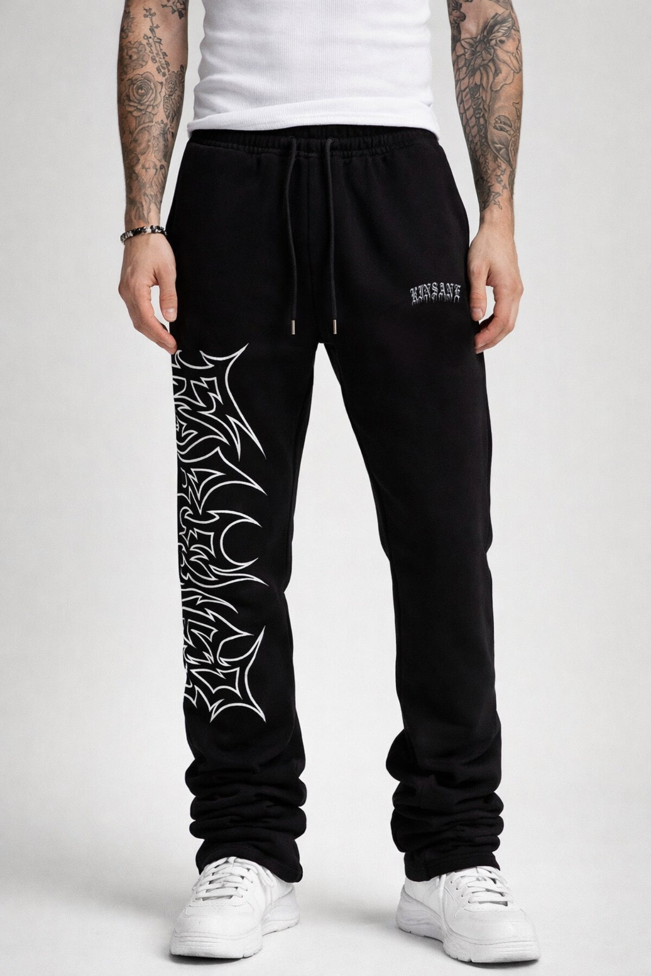 Guy wearing black stacked sweatpants with white outlined tribal lettering reading “forever” on the left side and white old English style lettering reading “KINSANE” on the right side 