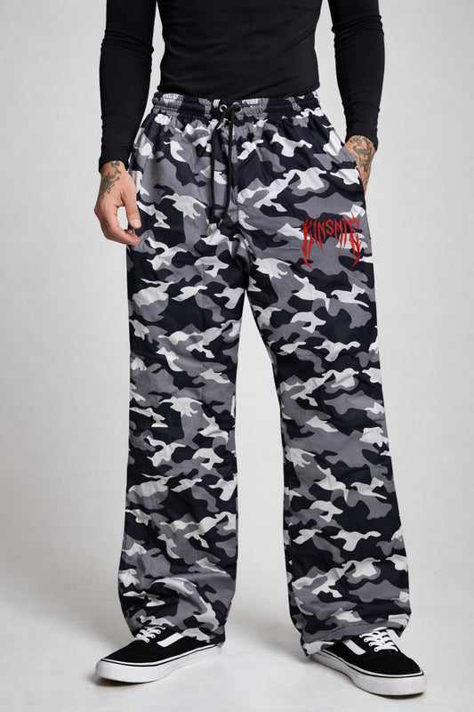Man wearing Camo baggy sweatpants with red tribal lettering on the right side reading “KINSANE” 