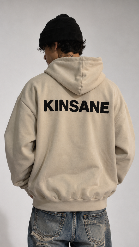 Back view of a man wearing a beige hoodie with black text reading “KINSANE” 