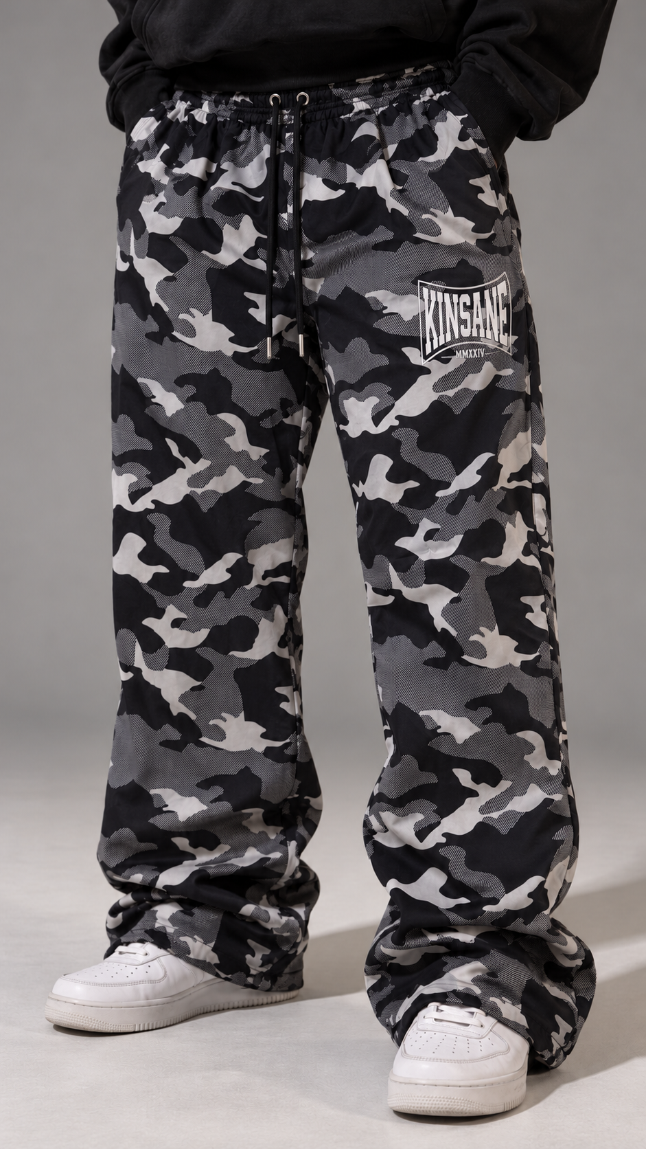 Man wearing Camo baggy sweatpants with white logo lettering on the right side reading “KINSANE MMXXIV” 
