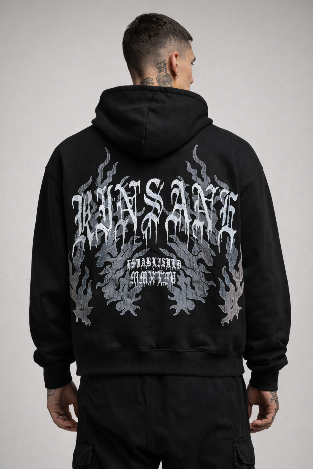 Back view of a man wearing a black hoodie with grey blue flames and white text reading “KINSANE ESTABLISHED MMXXIV” 