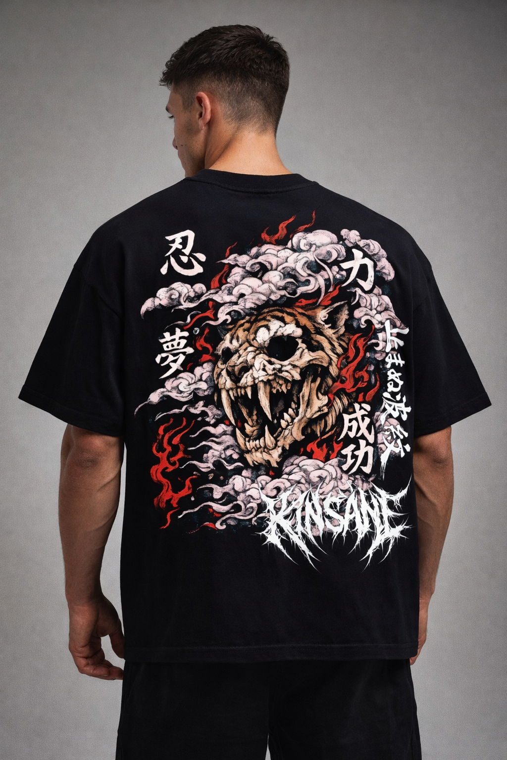 Back view of a man wearing a black T-shirt with a tiger skull design surrounded by red flames and white Japanese style smoke and Japanese text and white text reading “KINSANE” 