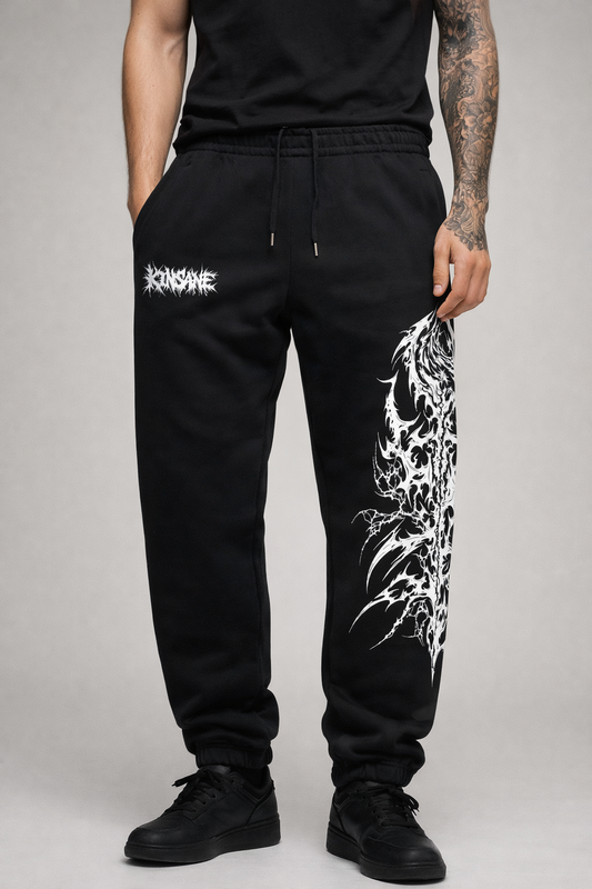 Man wearing Black cuffed joggers with white chaotic lettering reading “KINSANE” on the left side and white tribal designs on the right side leg