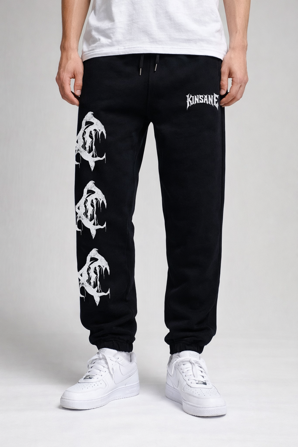 Man wearing Black cuffed joggers with 3 white logos stacked on the left side leg and white lettering on the right reading “KINSANE” 