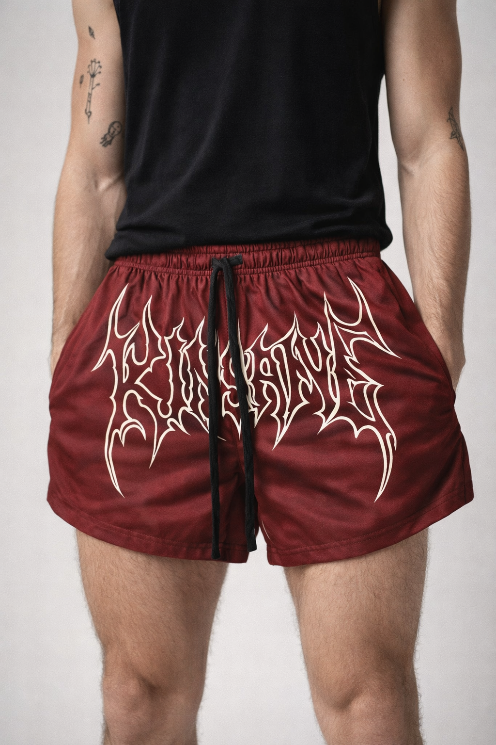 Man wearing Maroon athletic shorts with black drawstrings and white outlined lettering across the front reading “KINSANE” 