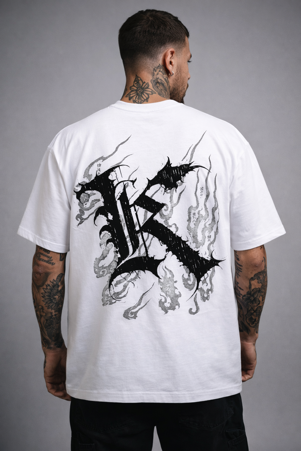 Back view of man wearing a white T-shirt with a black logo displaying black Japanese style flames and a black letter “K” and various Japanese text 