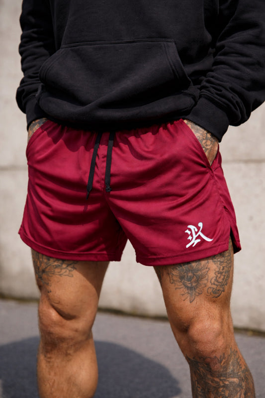 Guy wearing Maroon athletic shorts with black drawstrings and a white logo of the letter “K” on the left leg 