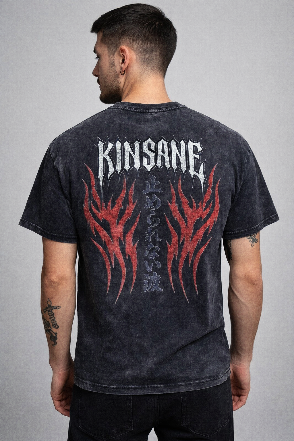 Back view of a man wearing a black acid washed t-shirt with red flames and white spiked lettering reading “KINSANE” and black Japanese lettering translating to “UNSTOPPABLE FLAME” 
