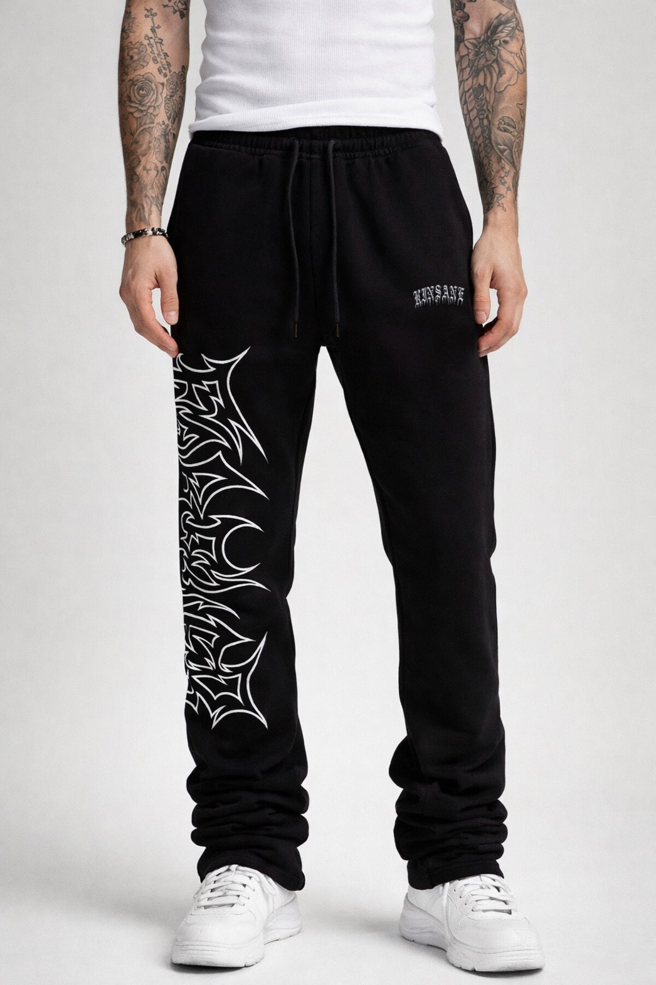 Guy wearing black stacked sweatpants with white outlined tribal lettering reading “forever” on the left side and white old English style lettering reading “KINSANE” on the right side 