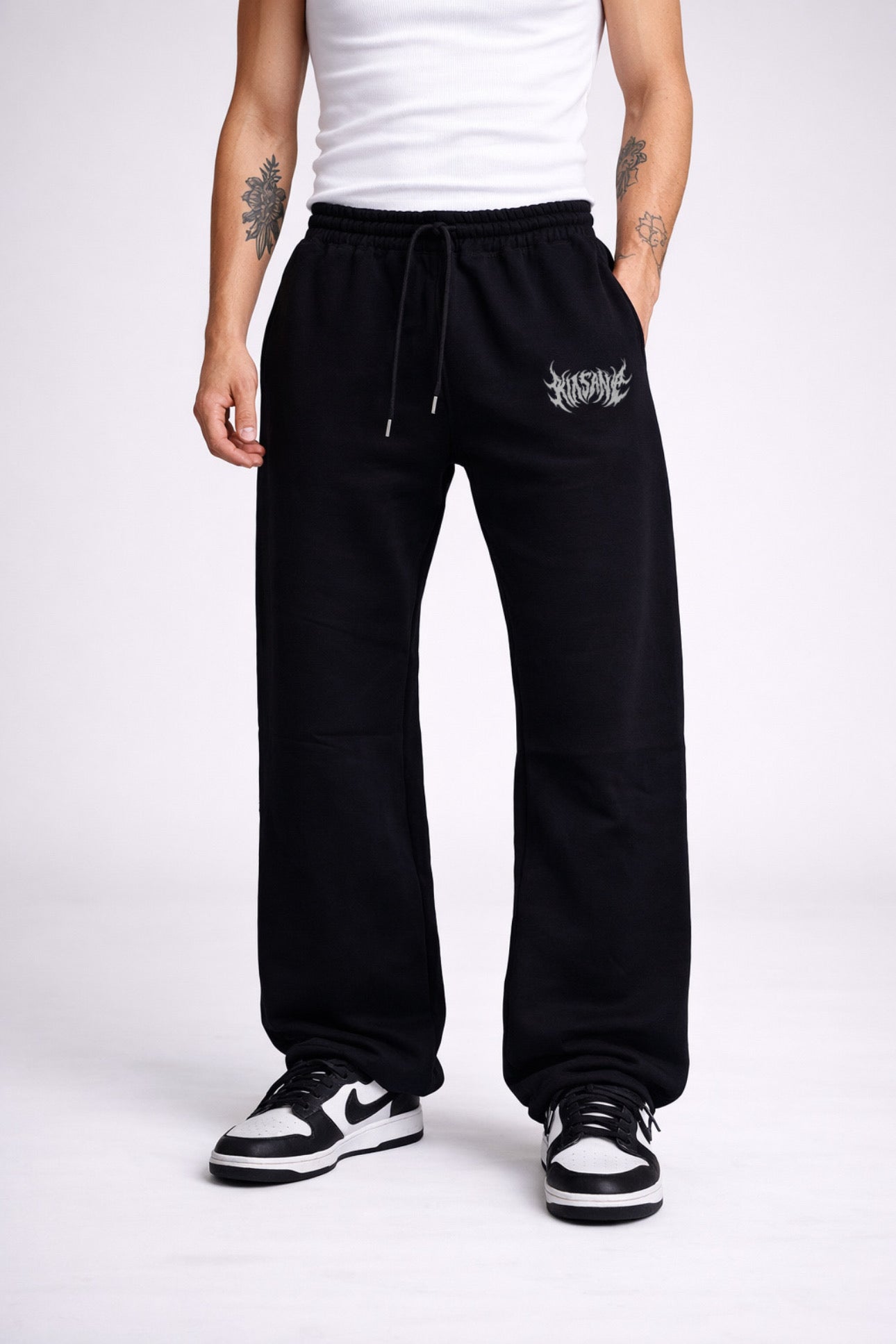 Man wearing Black stacked sweatpants with white lettering reading “KINSANE” on the left leg 