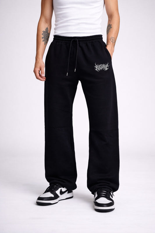 Man wearing Black stacked sweatpants with white lettering reading “KINSANE” on the left leg 