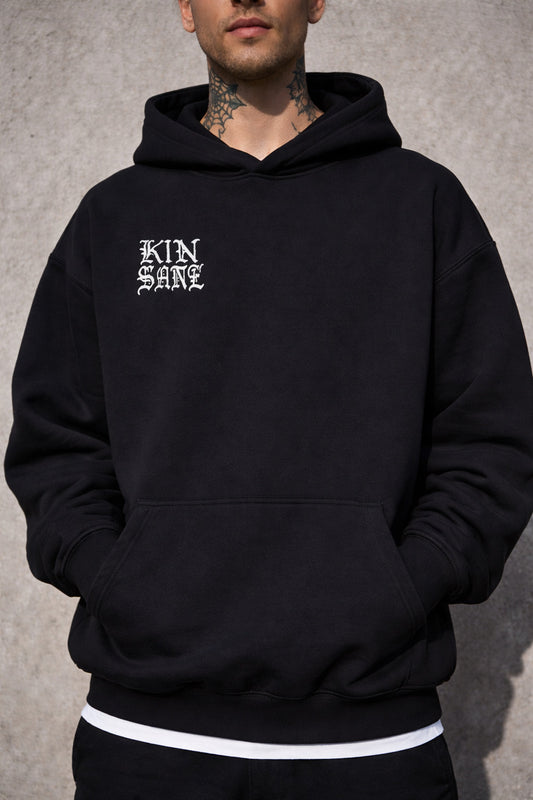 Man wearing a Black hoodie with silver text reading “KINSANE” 
